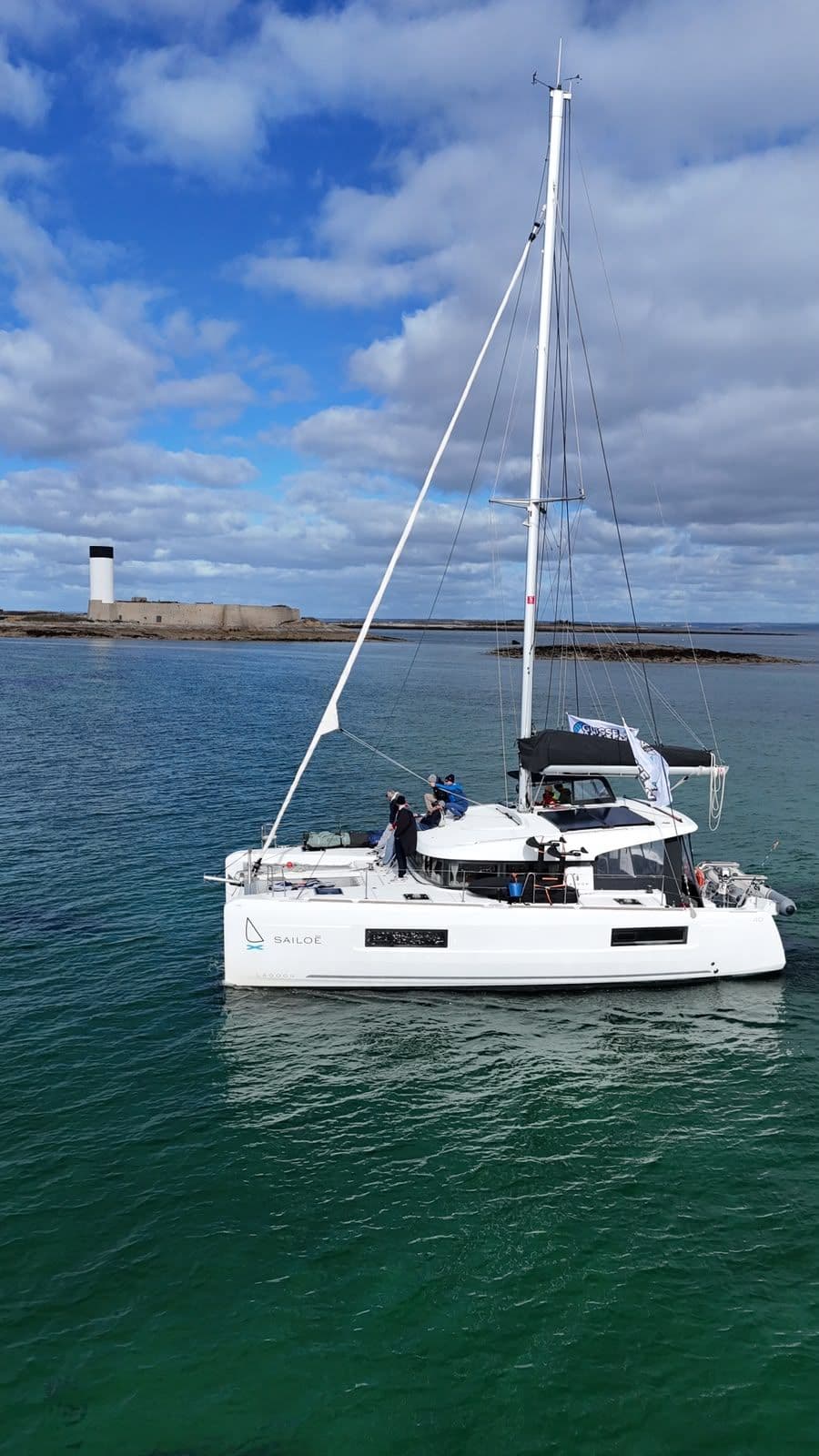 Bateau vu du ciel longeant un phare, sur une eau verte